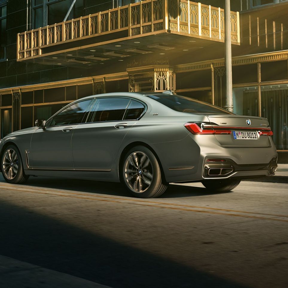 BMW M760Li xDrive со V12 мотор BMW M760Li xDrive стои во страничен заден поглед пред облакодери во урбана средина.