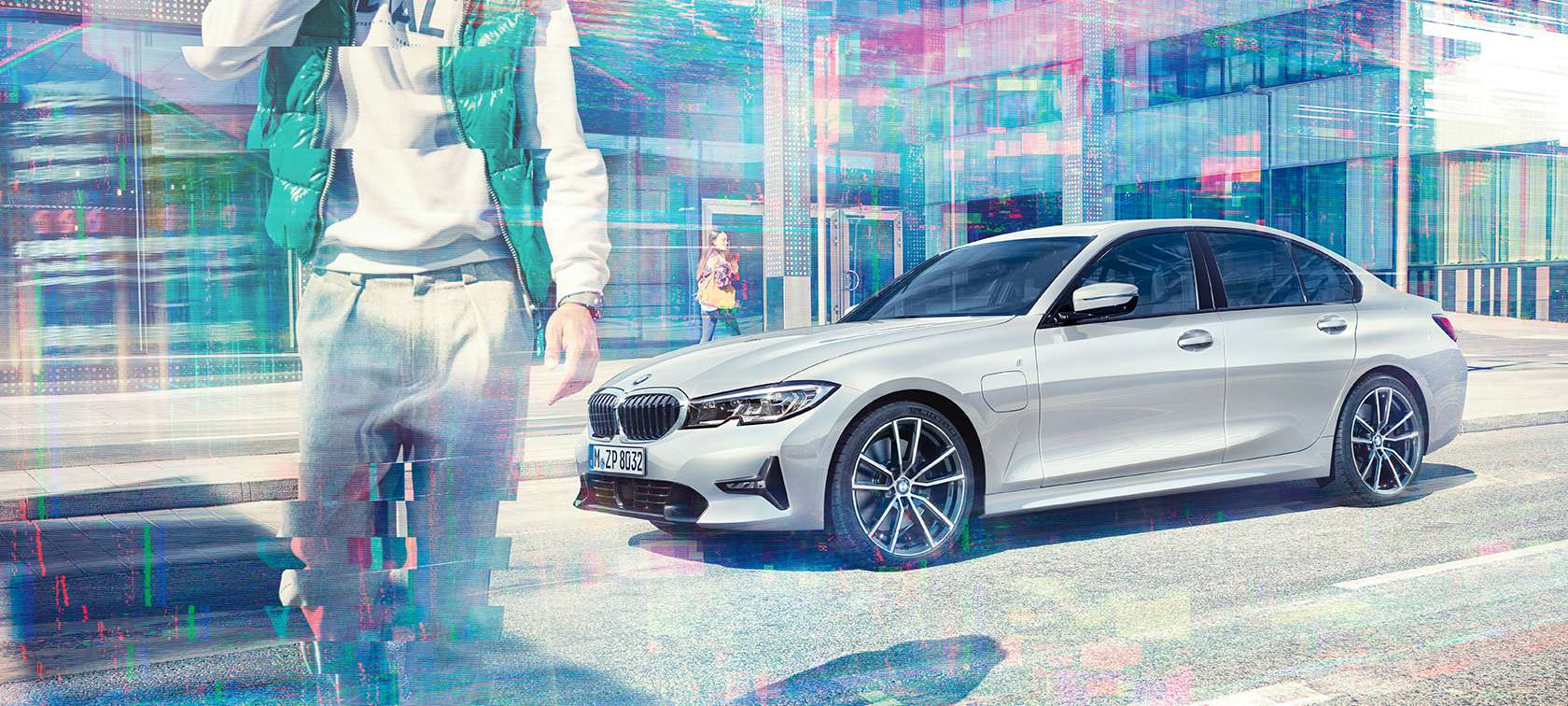 BMW Серија 3 Седан, страничен кадар на BMW 330e Тричетвртински страничен кадар на BMW 330e Седан во мирување пред урбана зграда од стакло и минувачи.