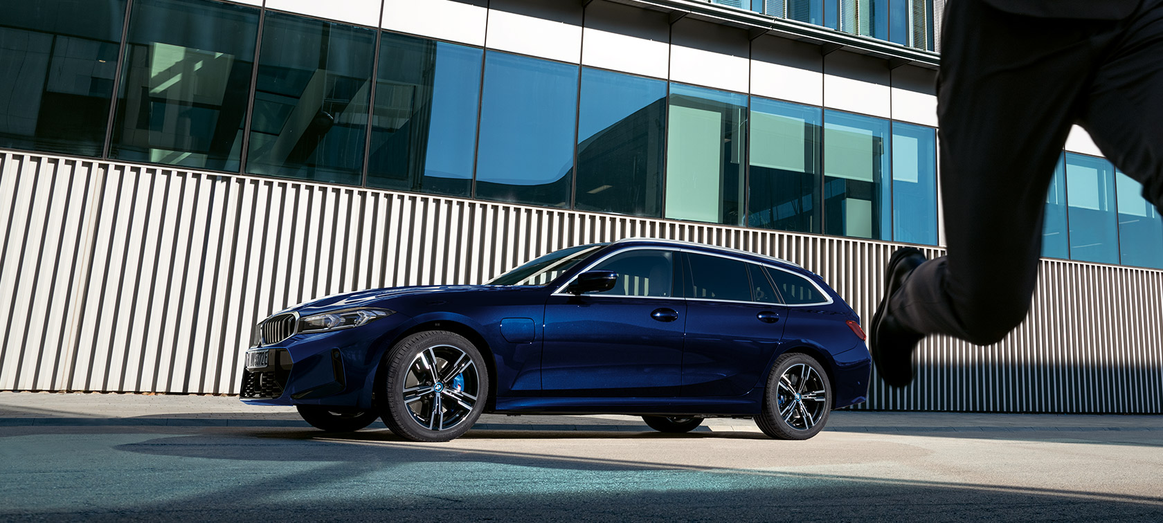 BMW Серија 3 Touring LCI G21 тричетвртински поглед одзади додека стои пред зграда BMW Серија 3 Touring LCI G21 Tansanit Blue II сина боја тричетвртински поглед одзади додека стои пред зграда