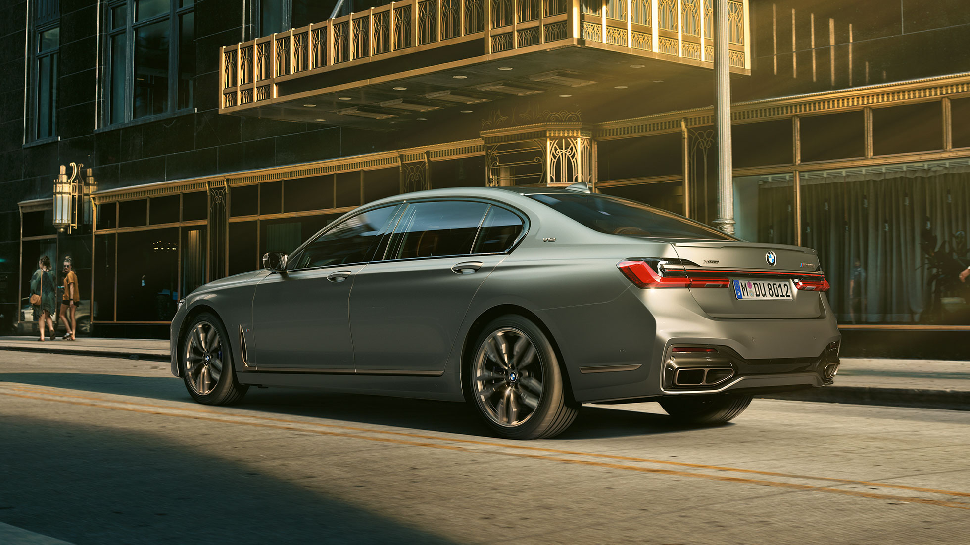 BMW M760Li xDrive со V12 мотор BMW M760Li xDrive стои во страничен заден поглед пред облакодери во урбана средина.