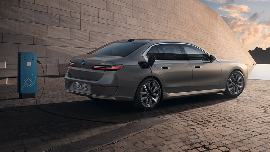 BMW i7 Седан G70 3/4 страничен поглед одзади BMW i7 Седан G70 BMW Individual Oxid grey сива металик боја 3/4 страничен поглед одзади на станица за полнење