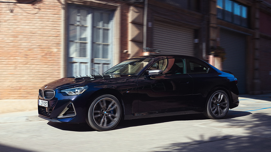 Тричетвртински страничен поглед BMW M240i xDrive Coupé G42 2021 BMW Серија 2 Coupé G42 2021 Thundernight металик тричетвртински страничен поглед паркиран пред магацин