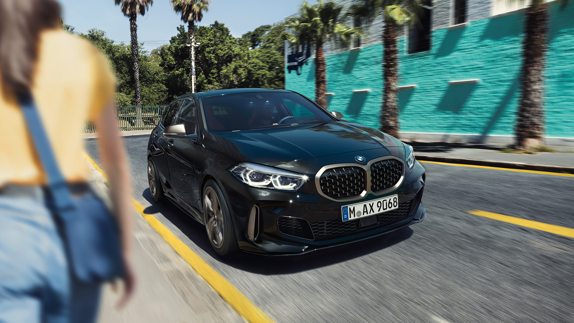 BMW M135i xDrive, тричетвртински приказ однапред BMW M135i xDrive во Black Sapphire црна металик боја, тричетвртински приказ однапред со жена во предниот дел.