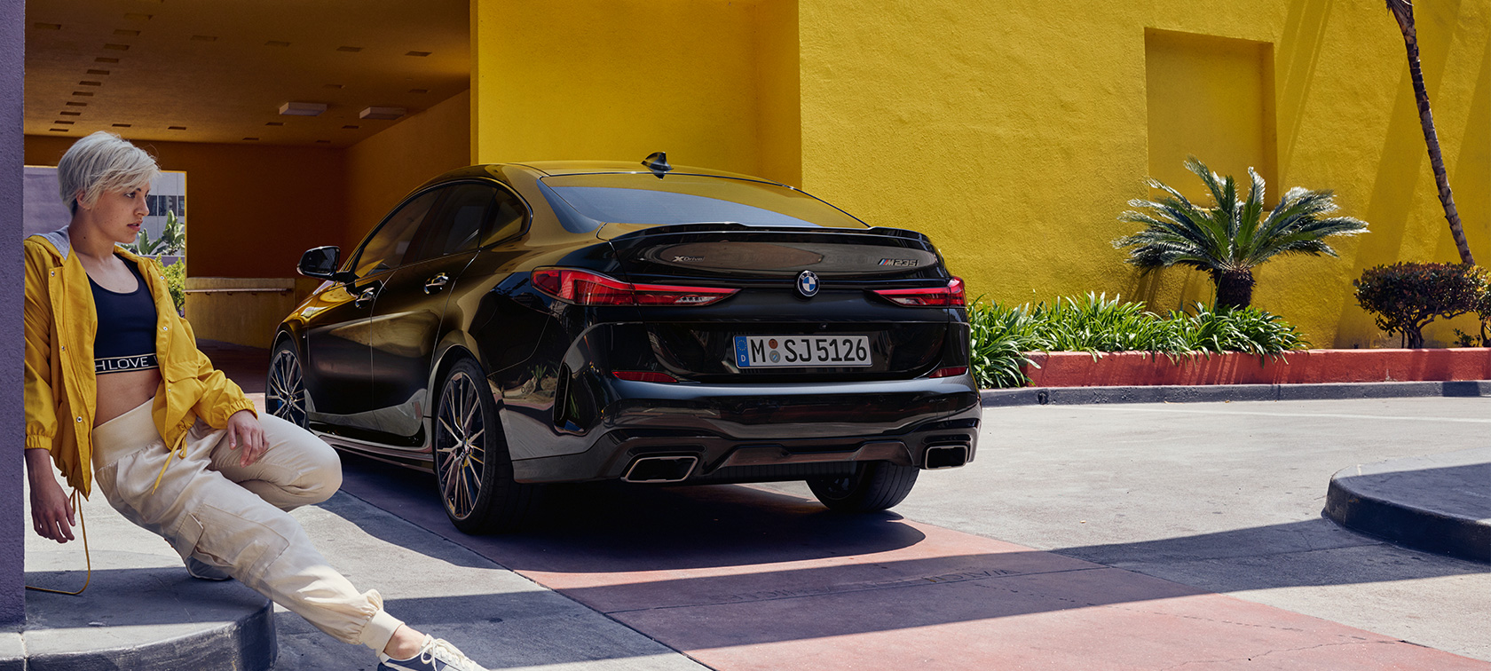 BMW M235i xDrive Gran Coupé три-четвртини страничен поглед BMW M235i xDrive Gran Coupé Black Sapphire металик F44 три-четвртини страничен поглед со жена во позадина