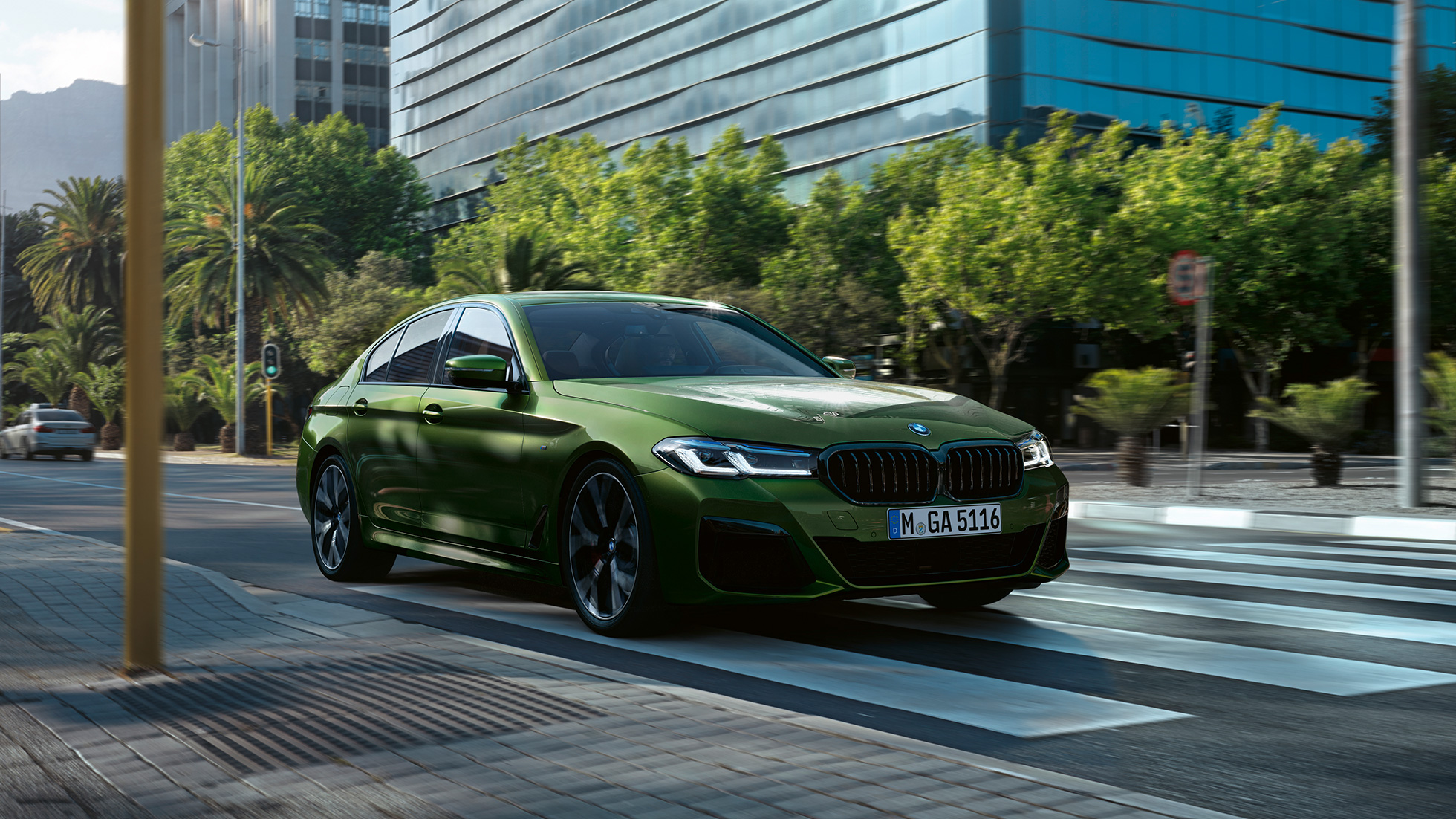BMW M550i xDrive Sedan G30 LCI Facelift 2020 three-quarter front view driving BMW M550i xDrive Sedan G30 LCI Facelift 2020 BMW Individual Verde Ermes metallic three-quarter front view driving downtown