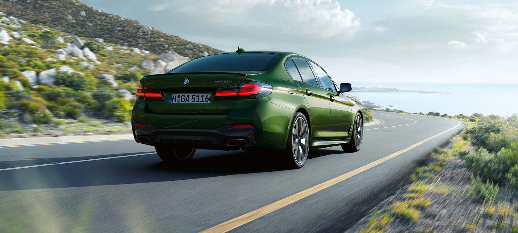 BMW M550i xDrive Sedan G30 LCI Facelift 2020 three-quarter rear view driving BMW M550i xDrive Sedan G30 LCI Facelift 2020 BMW Individual Verde Ermes metallic three-quarter rear view driving