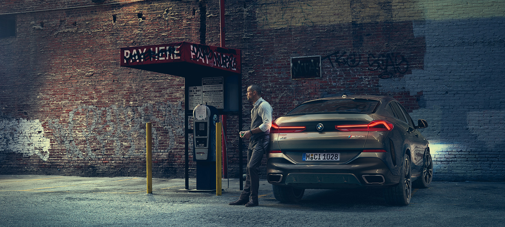 Заден дел од BMW X6 M50i. Човек потпрен на задниот дел од BMW X6 M50i.