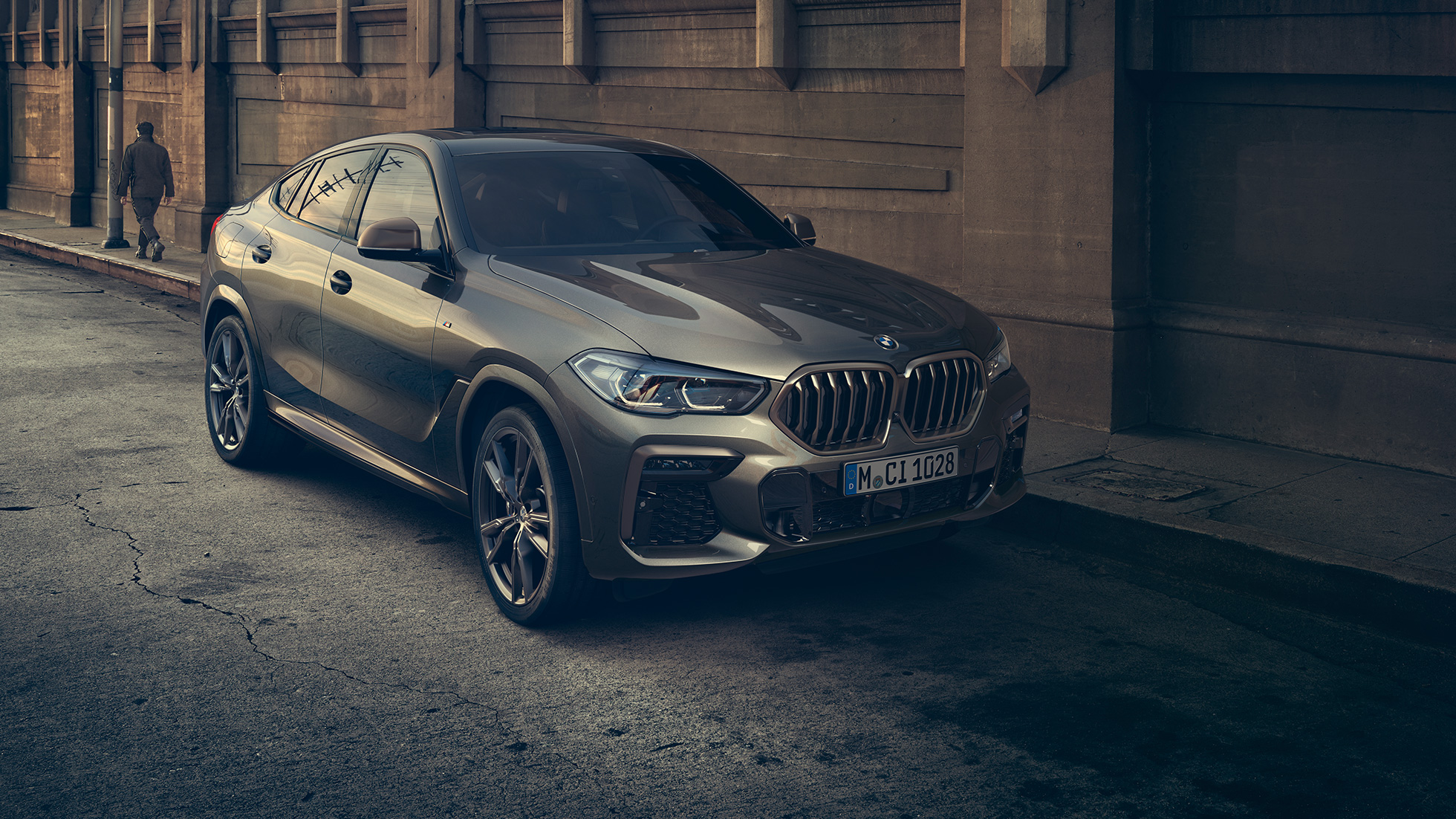 BMW X6 M50i во место. BMW X6 M50i тричетвртински приказ однапред пред урбана заднина.