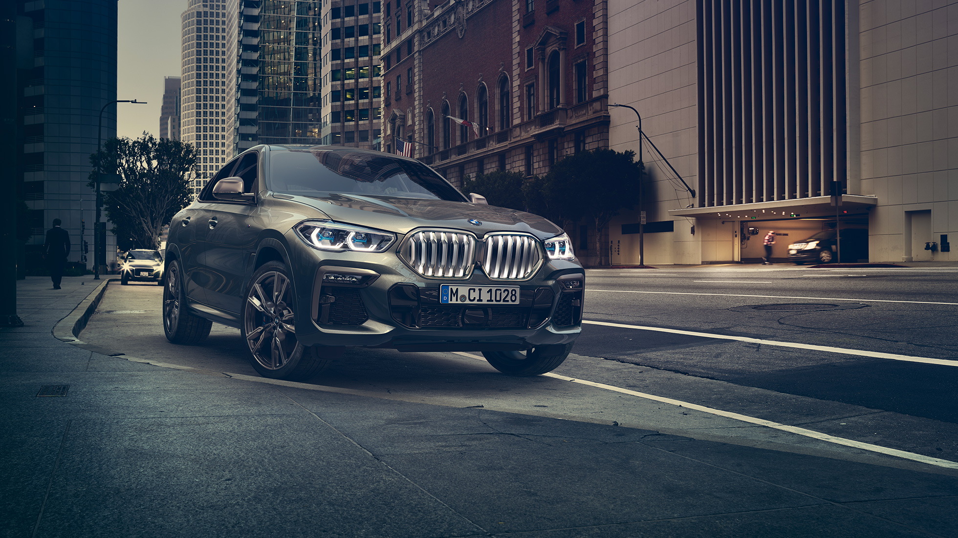 BMW X6 M50i во место. BMW X6 M50i тричетвртински приказ однапред пред урбана заднина.