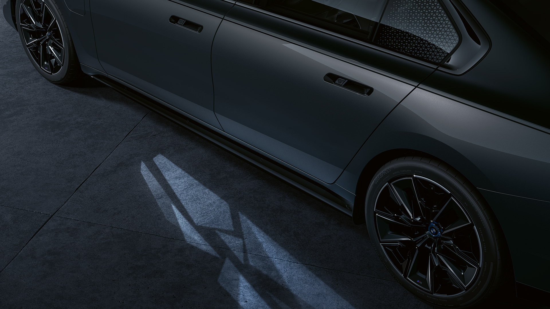 Концепт на осветлување BMW M760e xDrive Седан G70 Концепт за осветлување BMW M760e xDrive Седан G70 BMW Individual во две нијанси Black Sapphire црна металик каросерија BMW Individual Dravite Grey сива металик боја страничен поглед одблизу со вклучен Welcome Light Carpet