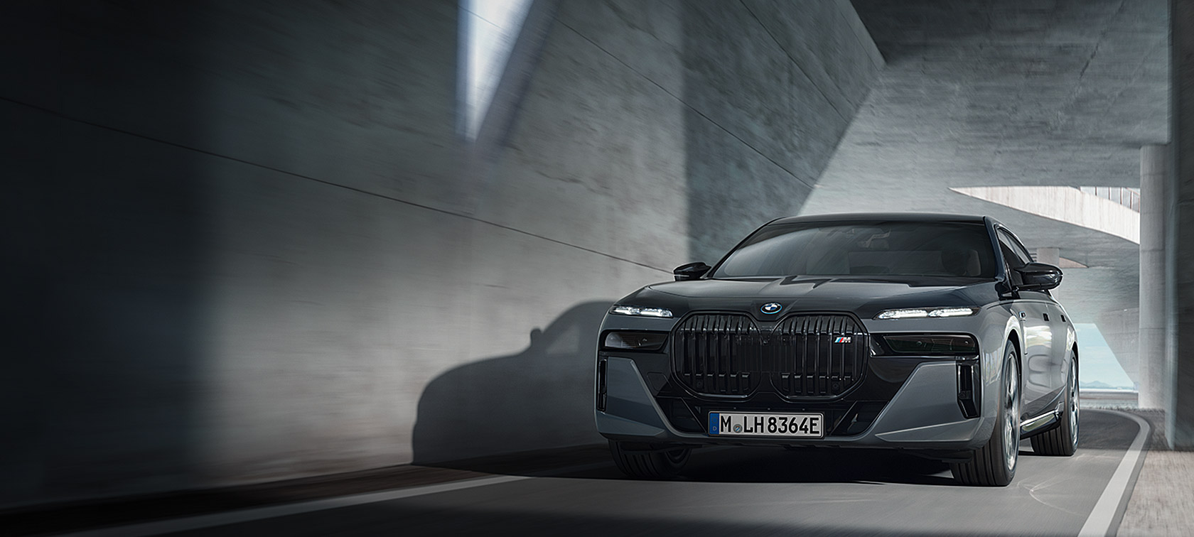 BMW M760e xDrive Седан G70 M Performance пакет BMW Individual во две нијанси Black Sapphire црна металик каросерија BMW Individual Dravite Grey сива металик боја тричетвртински поглед однапред стои во отворена бетонска структура со скали