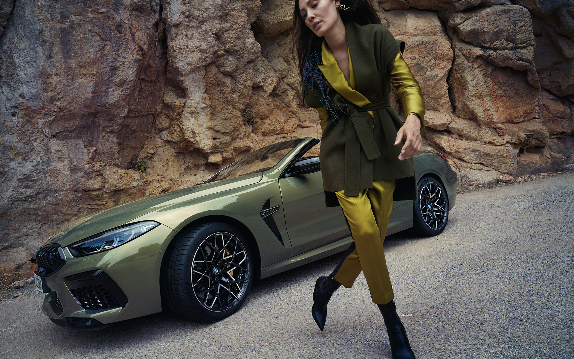 BMW M8 Competition кабриолет F91 LCI 2022 тричетвртински поглед однапред паркиран пред каменест предел BMW M8 Competition кабриолет F91 LCI Facelift 2022 BMW Individual Brass металик, тричетвртински поглед однапред, паркиран пред каменест предел со женски модел