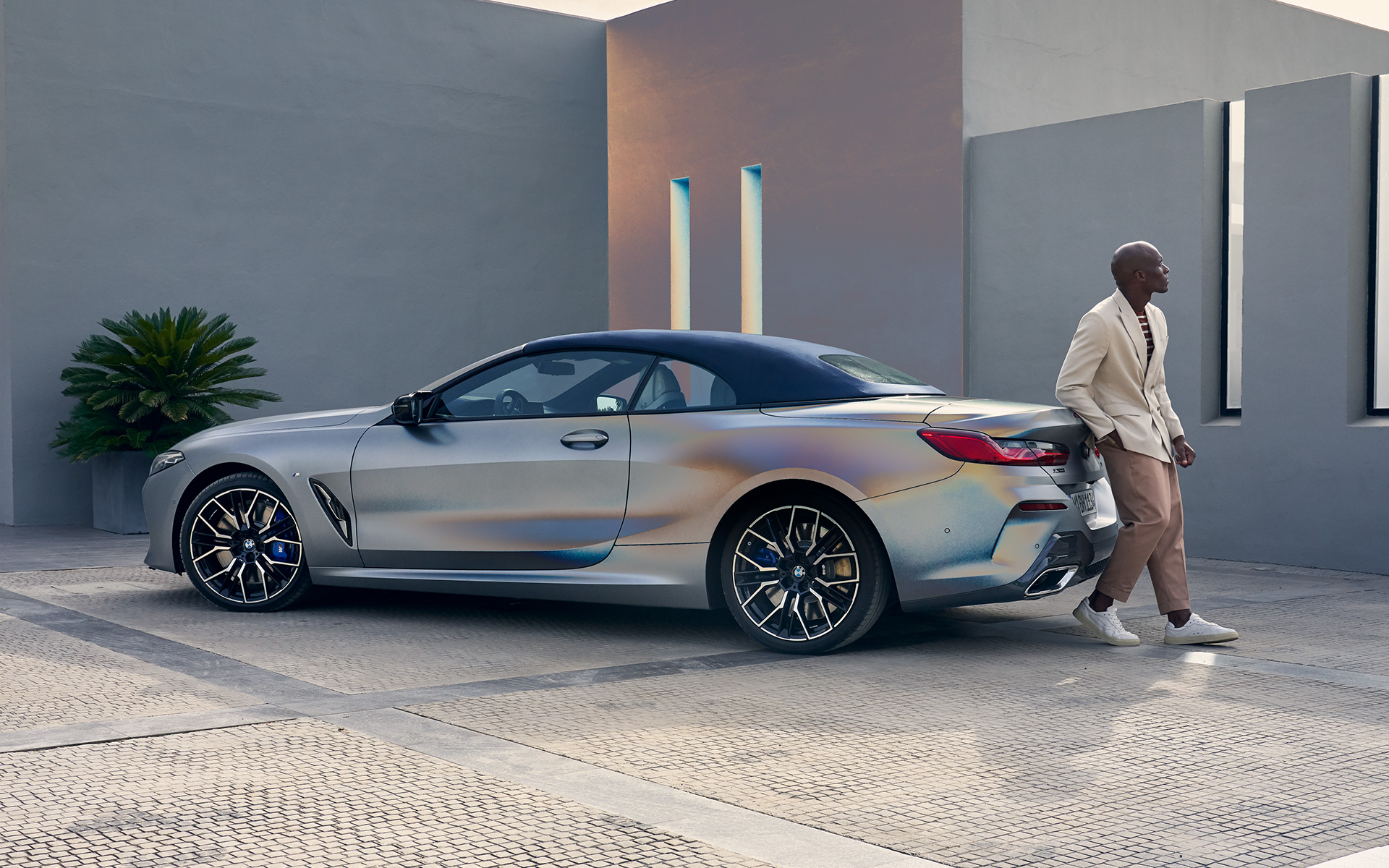 Тричетвртински поглед одназад на BMW M850i xDrive кабриолет G14 LCI Facelift 2022 BMW M850i xDrive кабриолет G14 LCI Facelift 2022 BMW Individual Frozen Pure Grey металик боја, тричетвртински поглед одназад и машки модел потпрен на возилото
