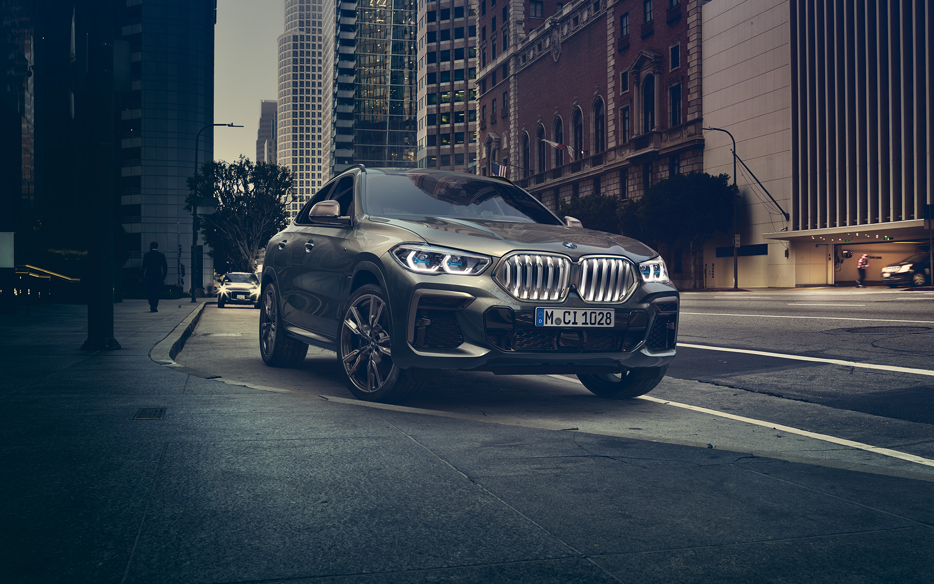BMW X6 M50i во три-четвртинска предна перспектива во стоење покрај урбан пејзаж G06 2018 SUV