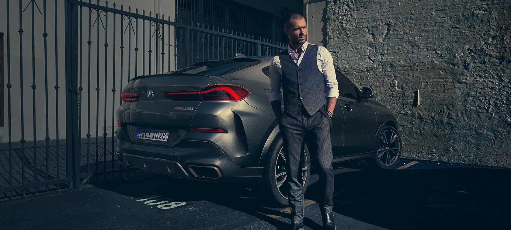 BMW X6 M50i во три-четвртински заден поглед G06 Човек застанат до BMW X6 M50i G06 2018 SUV во три-четвртински заден поглед