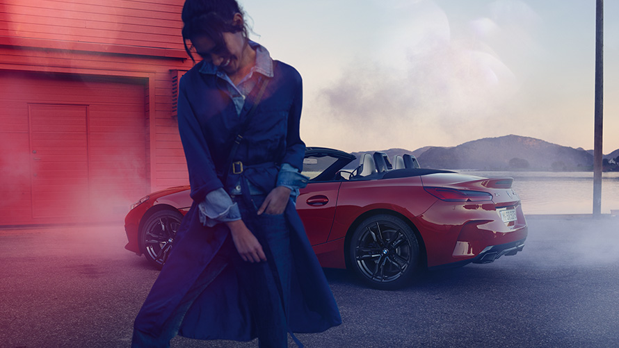BMW Z4 M40i Roadster G29 со отворен мек покрив BMW Z4 M40i Roadster G29 тричетвртински поглед одзади со отворен мек покрив и жена во преден план