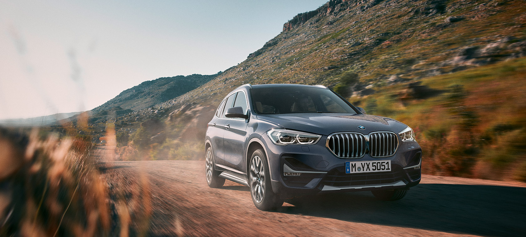 BMW X1, тричетвртински приказ од напред при возење сред планински пејзаж.