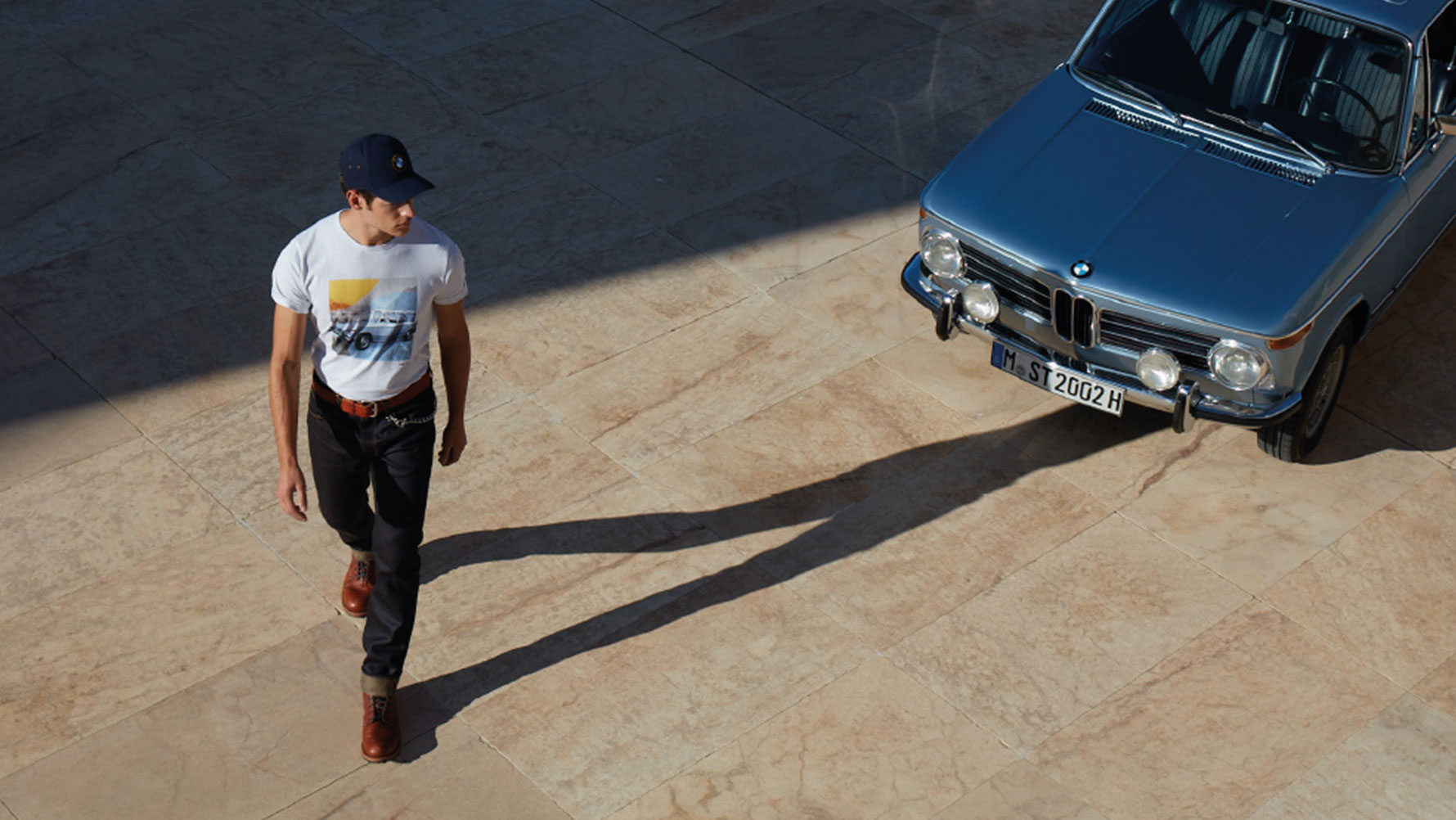 A man wearing a BMW Classic Men’s T-shirt is shown admiring a classic BMW. A man wearing a BMW Classic Men’s T-shirt is shown admiring a classic BMW.