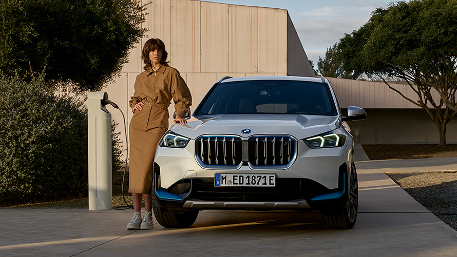 Маж во петролеј-зелен капут пред BMW iX3 BMW iX3 G08 2021 Маж во петролеј-зелен капут пред BMW iX3 G08 2021 страничен поглед полнење во гаража
