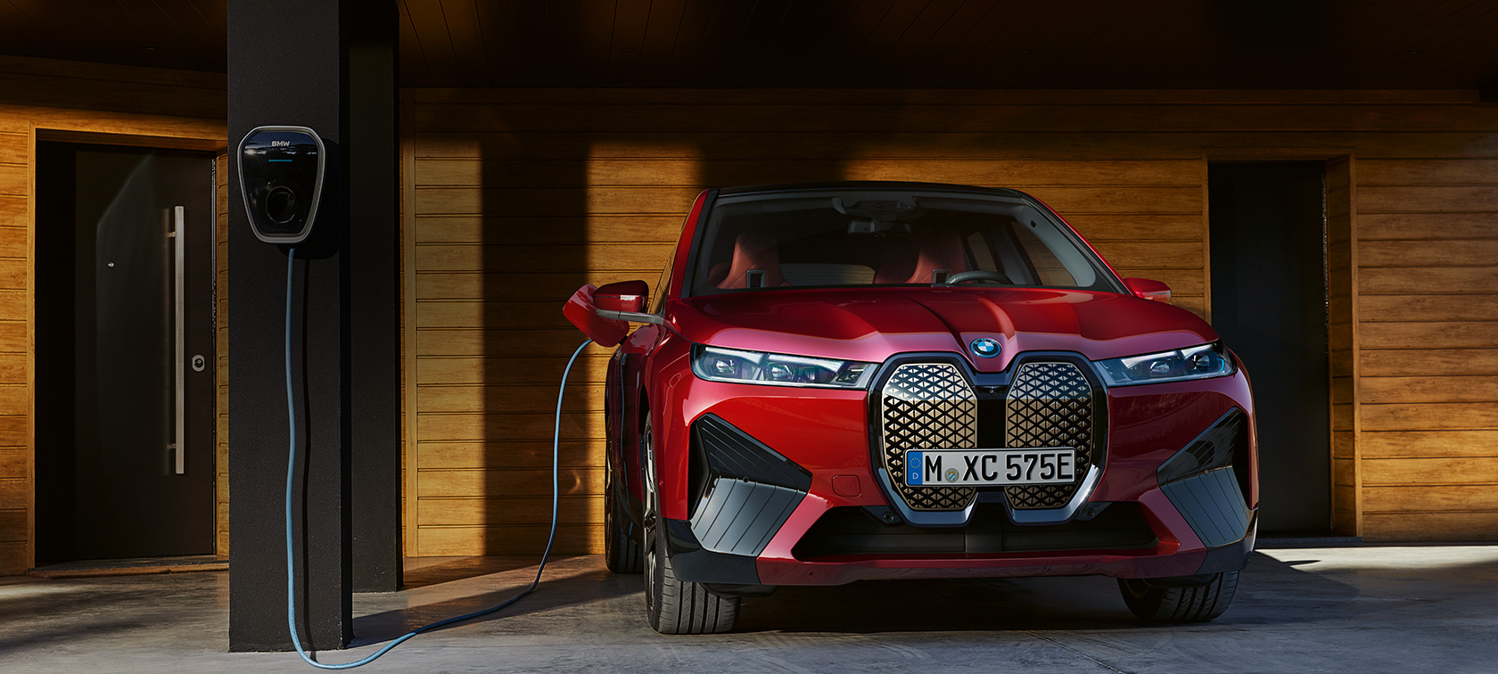 BMW iX дома со wallbox поглед однапред BMW iX дома со wallbox во гаража со дрвен ѕид поглед однапред